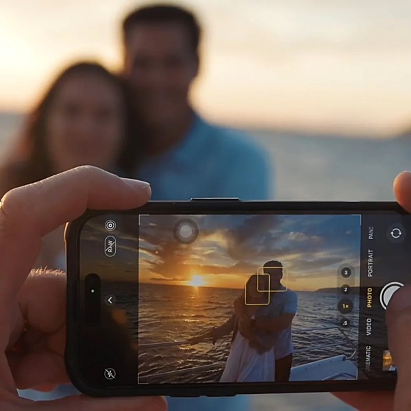 Smartphone capturing couple hugging at sunset by the ocean.