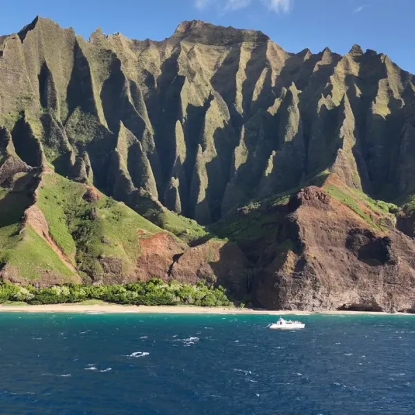 Dramatic cliffs with green and brown hues above a blue ocean and a small boat near the shore.