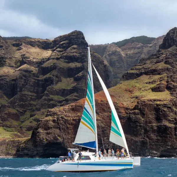 Sailboat with striped sails near rocky cliffs on a sunny day.