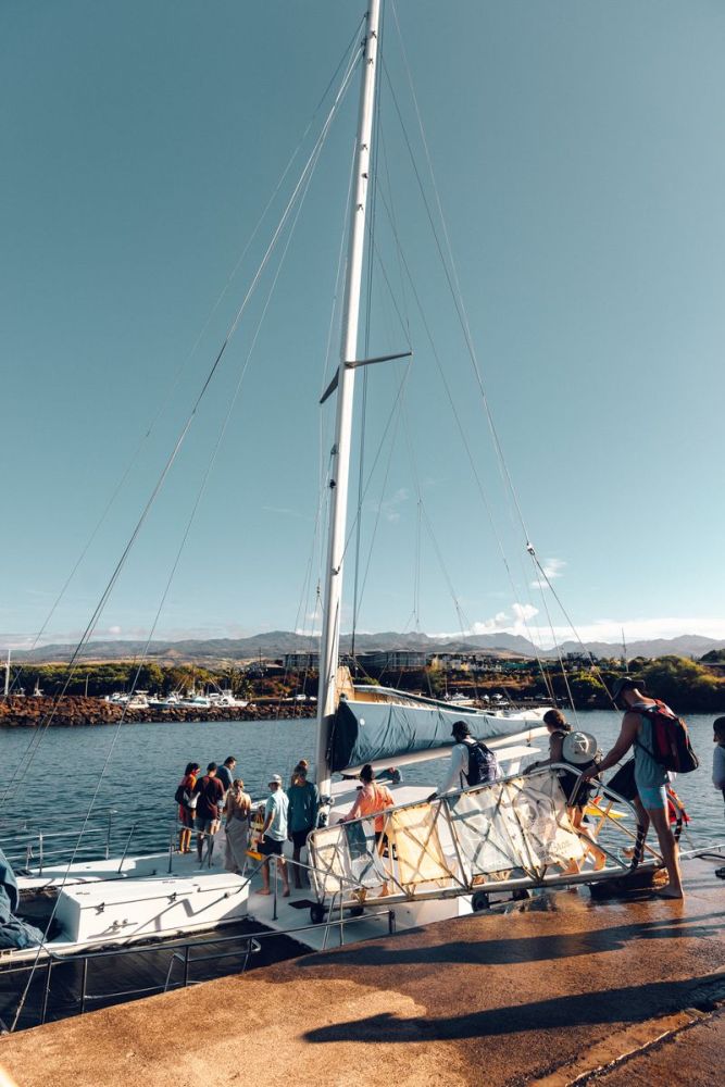 People boarding a sailboat at a dock under a clear blue sky.
