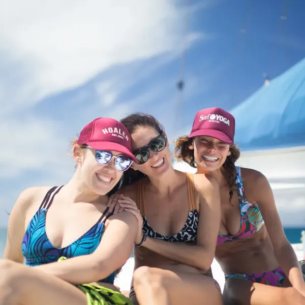Three women in swimwear and caps smiling on a boat under a clear sky.