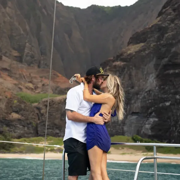 Couple kissing on a boat with rocky cliffs and ocean in the background.