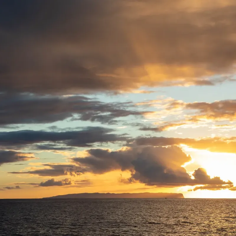 Sunset over the ocean with clouds and visible horizon.