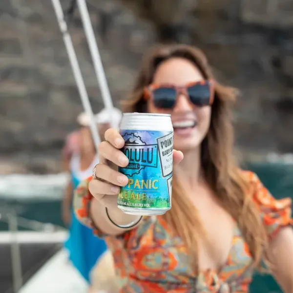 Woman on boat holding a can towards the camera, wearing sunglasses and an orange floral top.