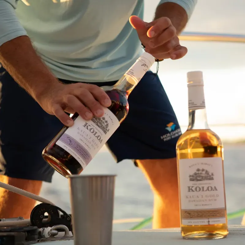 Person on a boat holding a bottle of Koloa rum, with another bottle and cup nearby.