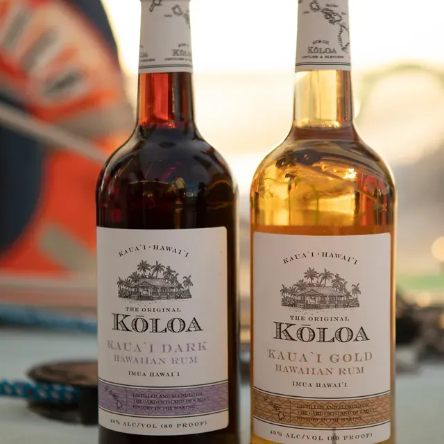Two bottles of Koloa Hawaiian rum, one dark and one gold, on a table outdoors.