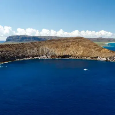 Aerial view of a crescent-shaped island surrounded by blue ocean under a clear sky.