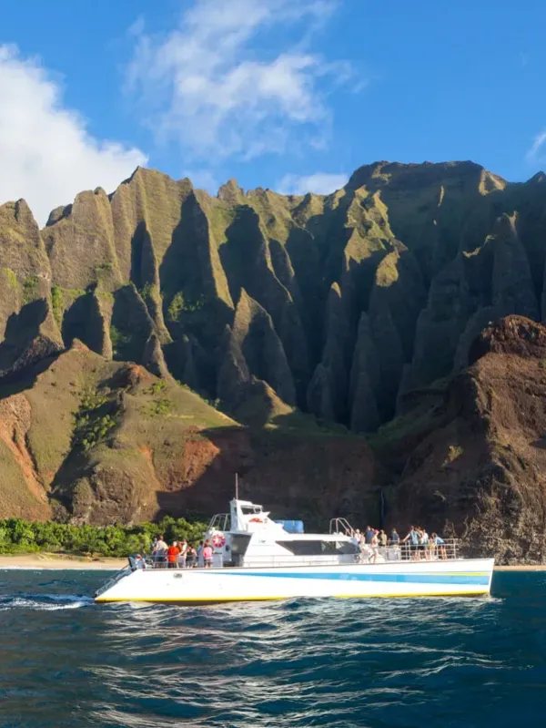 A boat on the ocean near dramatic, steep cliffs under a blue sky.
