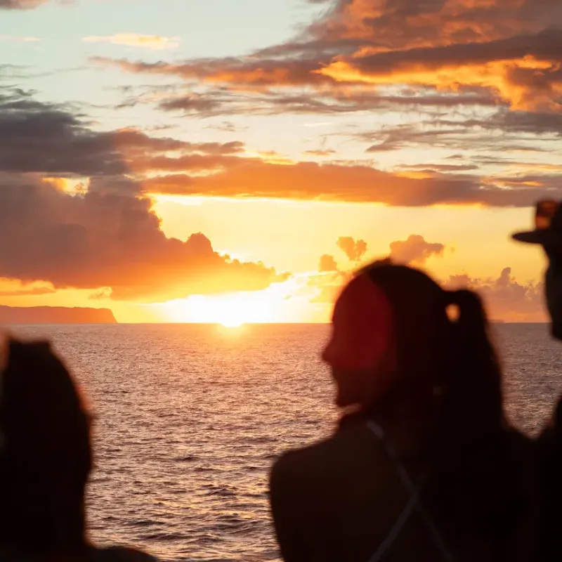 Silhouetted group of people watching a vibrant ocean sunset with clouds.