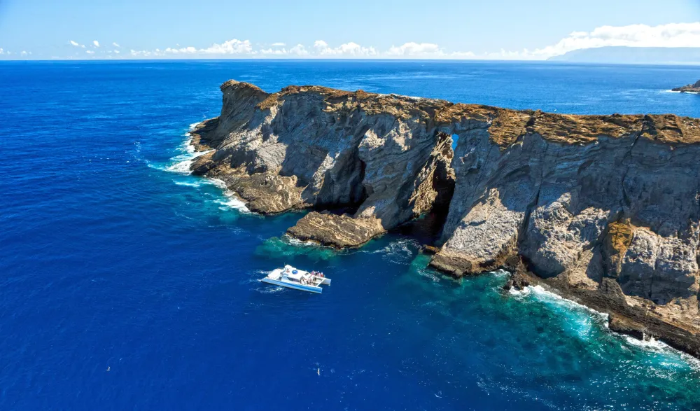 Aerial view of a boat near rugged cliffs and blue ocean under a clear sky.