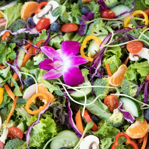 Colorful salad with various vegetables, fruits, and a purple flower centerpiece.