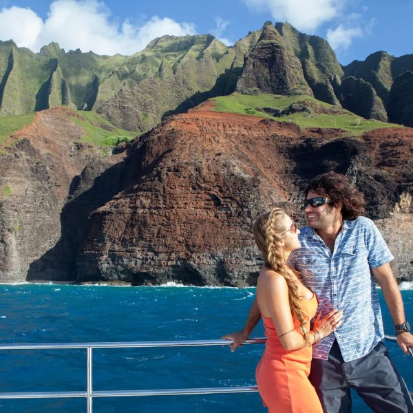 Couple on a boat with scenic cliffs and blue ocean in the background.