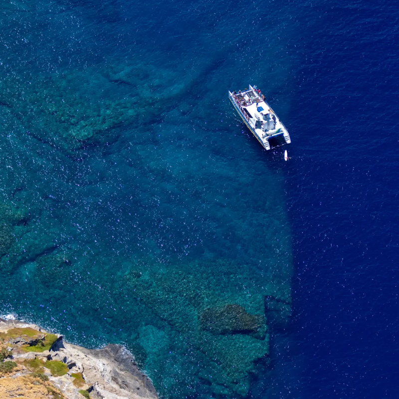 Aerial view of a white boat in clear blue water near a rocky coastline.